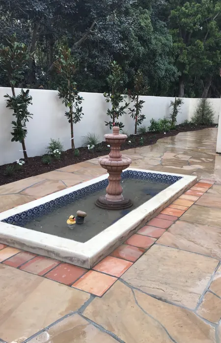 After: flagstone courtyard with a tiled fountain and new plantings along the wall