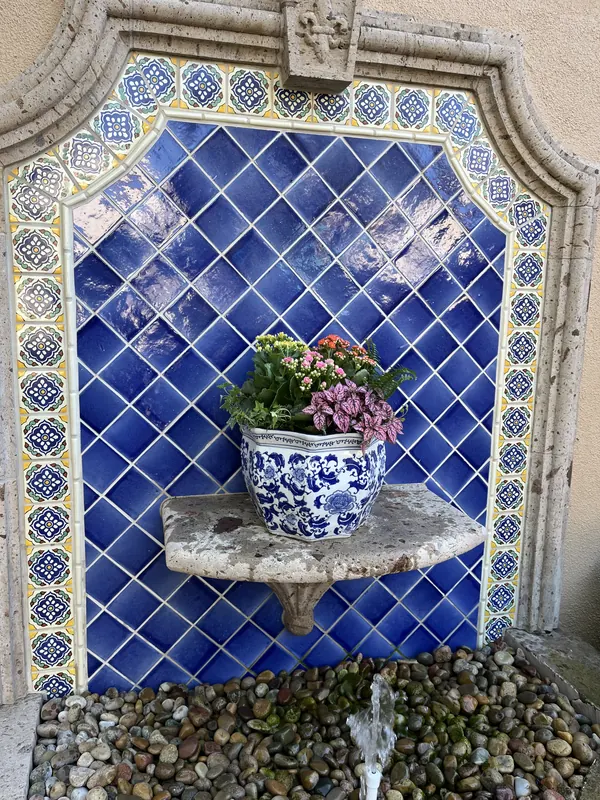 Blue and white pot of flowers set in a tiled wall fountain